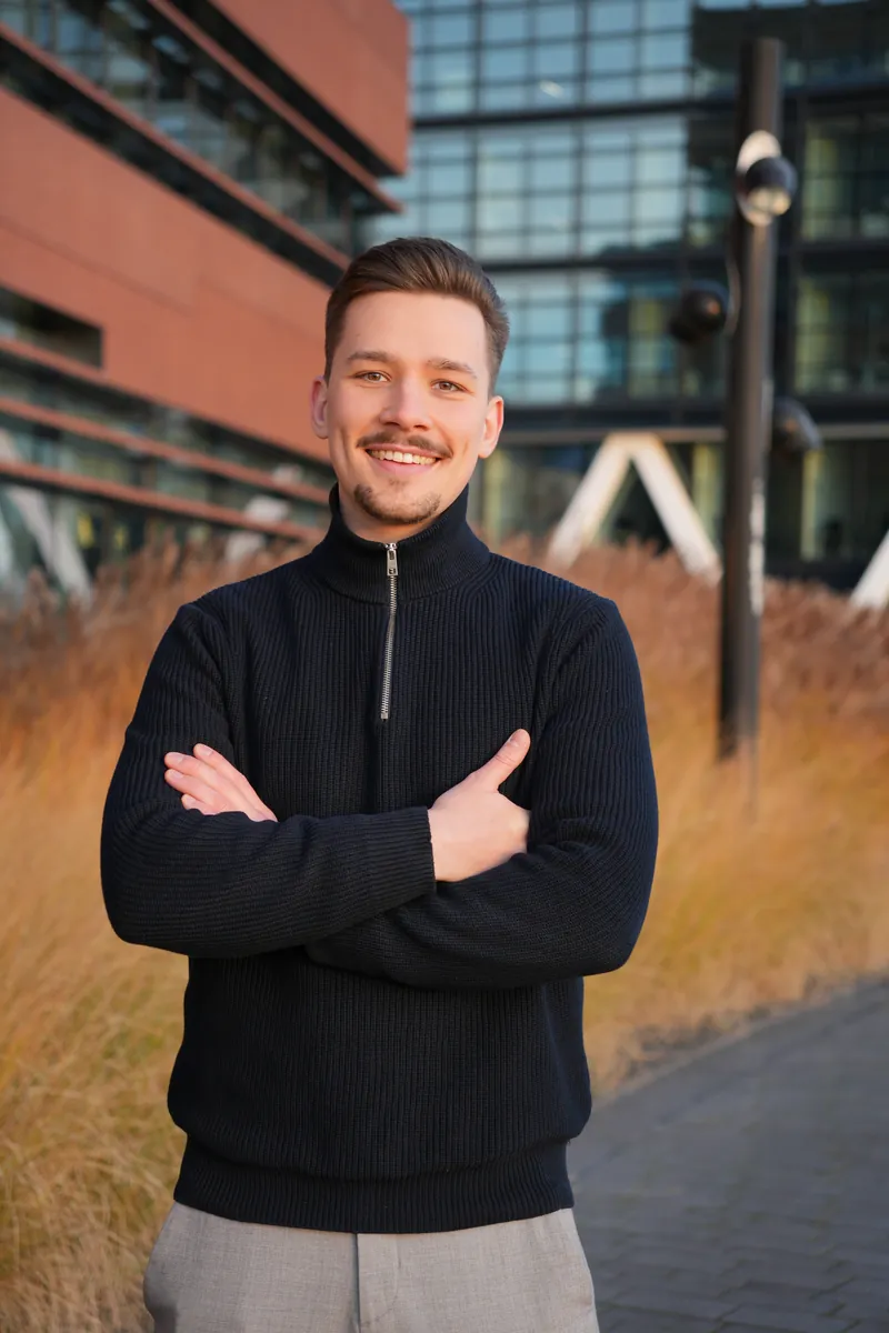 Tom Falz, Versicherungsmakler in Bremen, lächelnd mit verschränkten Armen vor einem modernen Bürogebäude